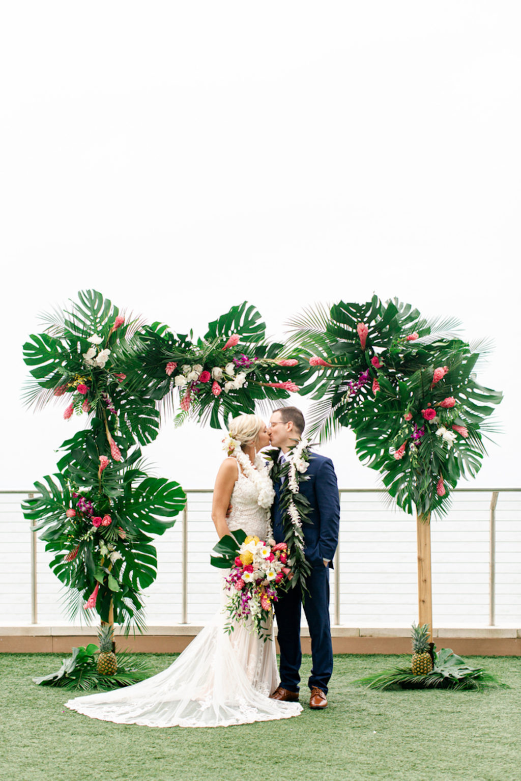 Tropical Elegant Waterfront Wedding Ceremony Decor, Bride Holding Lush and Colorful Bouquet and Groom Kiss Under Arch with Monstera Palm Tree Leaves, Pink Ginger, Purple Orchids, White Flowers | Tampa Bay Wedding Planner Special Moments Event Planner | Clearwater Beach Opal Sands Resort