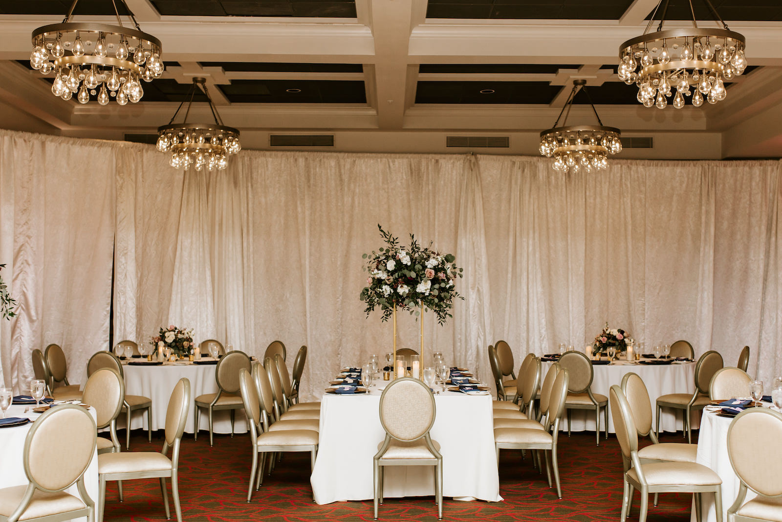 Indoor Hotel Ballroom Reception at St. Pete Wedding Venue The Birchwood | Ivory Pipe and Drape | Reception Tables with Gold Banquet Chairs and Ivory Table Linens | Tall Gold Metal Centerpiece Stand with Loose Natural Eucalyptus Greenery and Ivory and Pink Roses