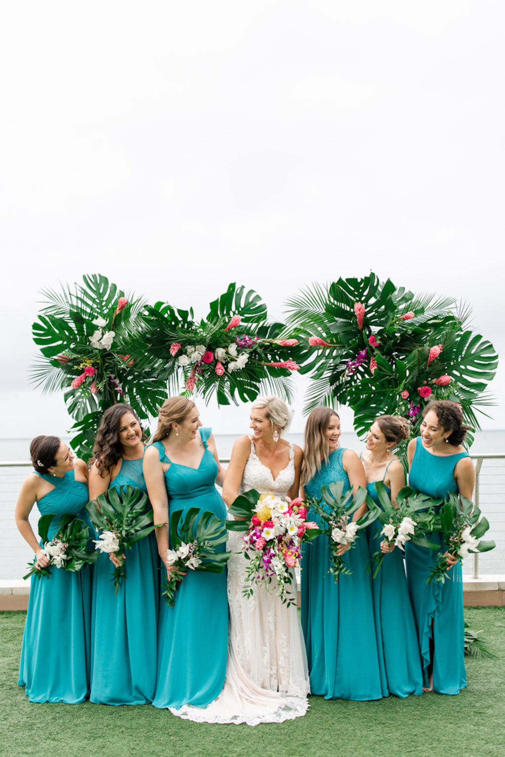 Tropical Elegant Waterfront Bridal Party Photo, Bridesmaids in Mix and Match Teal Dresses, Bride in Lace Wedding Dress Holding Colorful Lush Floral Bouquet, Arch with Monstera Palm Tree Leaves, Pink Ginger, Purple Orchids, White Flowers | Tampa Bay Wedding Planner Special Moments Event Planning