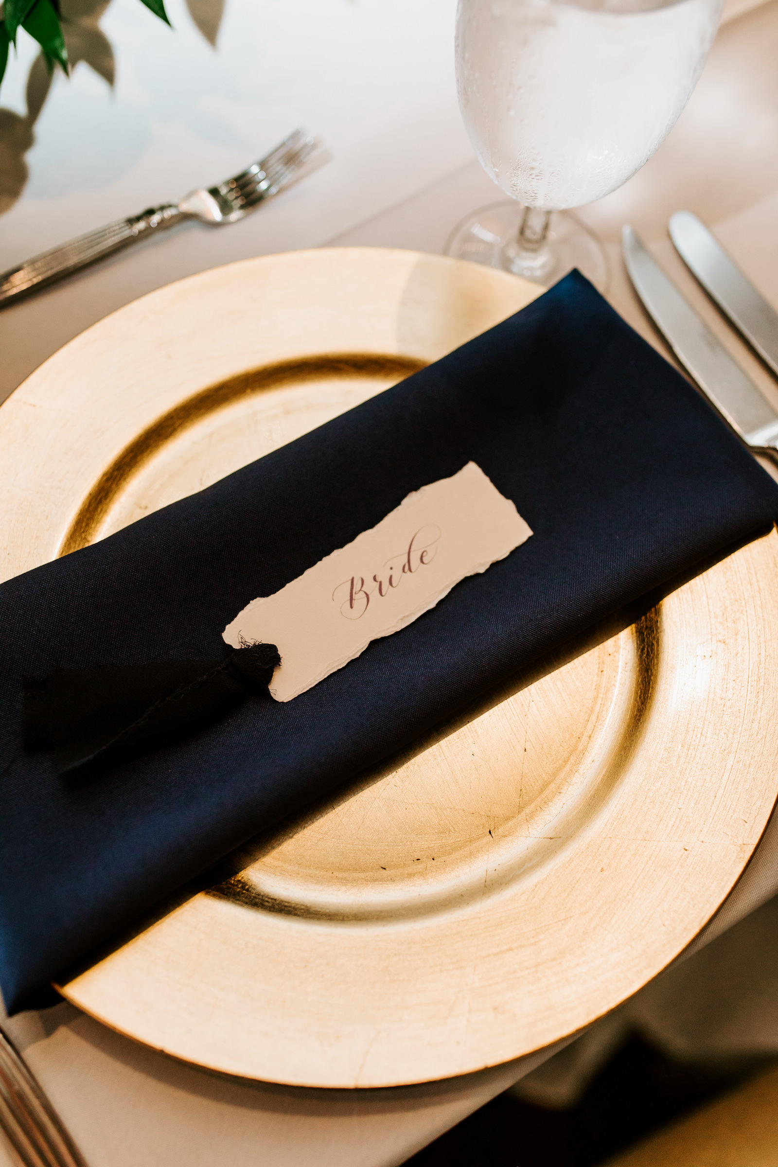 Wedding Place Setting with Gold Charger Plate and Navy Blue Napkin Wrap topped with Raw Deckle Edge Place Card