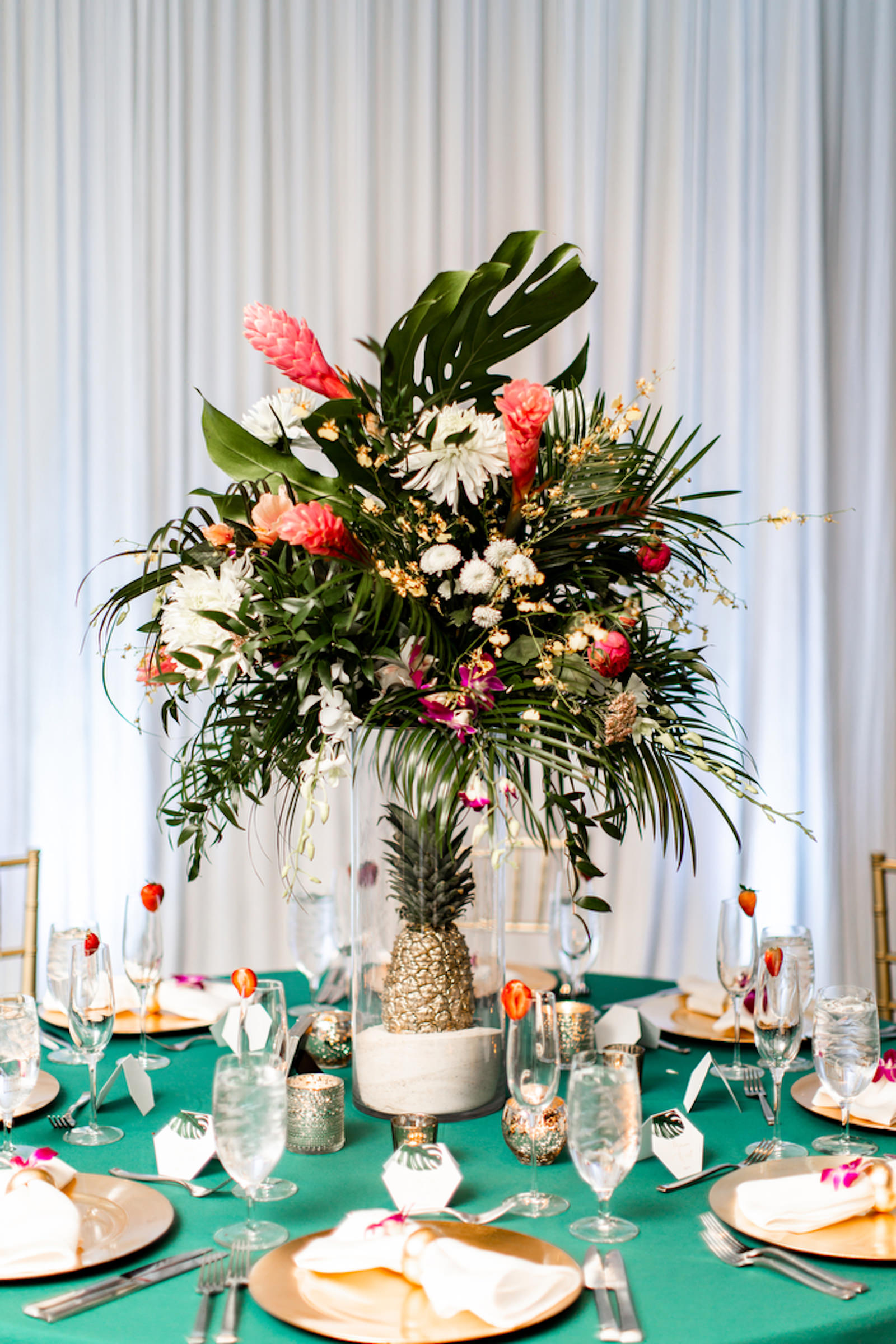Tropical Elegant Wedding Reception Decor, Teal Tablecloths, Gold Chargers, Tall Floral Centerpiece, Clear Hurricane Glass Vase with Sand and Gold Pineapple, Monstera and Palm Tree Leaves, Pink Ginger, Purple Orchids, White Florals Centerpiece | Tampa Bay Wedding Planner Special Moments Event Planning