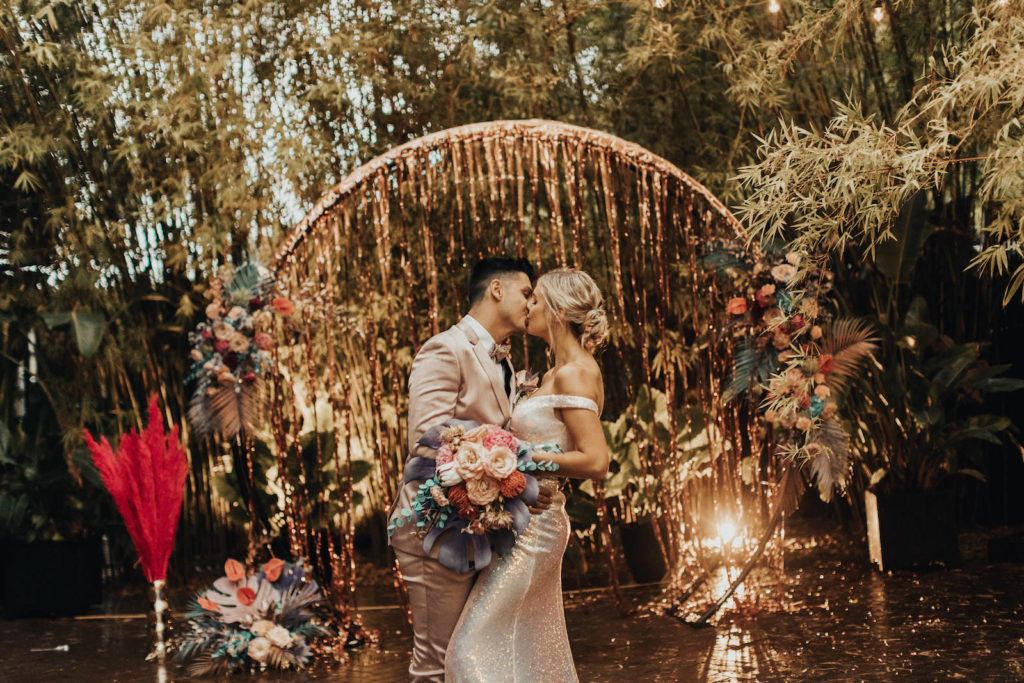 Iridescent Pastel 90's Wedding Inspiration | Wedding Arch Backdrop with Rose Gold Tinsel Curtain and Pastel Flower Arrangements with Painted Leaves | Bride and Groom Portrait with Blush Pink Suit and Shimmer Silver Wedding Dress | Downtown St. Pete Wedding Venue NOVA 535