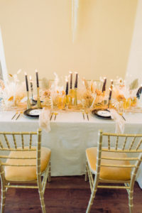 Trendy and Modern Boho Wedding Reception Tablescape Decor, Long Table with White Tablecloth, Gold Chiavari Chairs with Gold Velvet Cushions, White Floral Dried Preserved Flowers, Feathers and Foliage, Ivory Table Runner, Black Taper Candlesticks and Chargers | Tampa Bay Wedding Planner, Designer, Florist John Campbell Weddings | Tabletop Rentals Kate Ryan Event Rentals