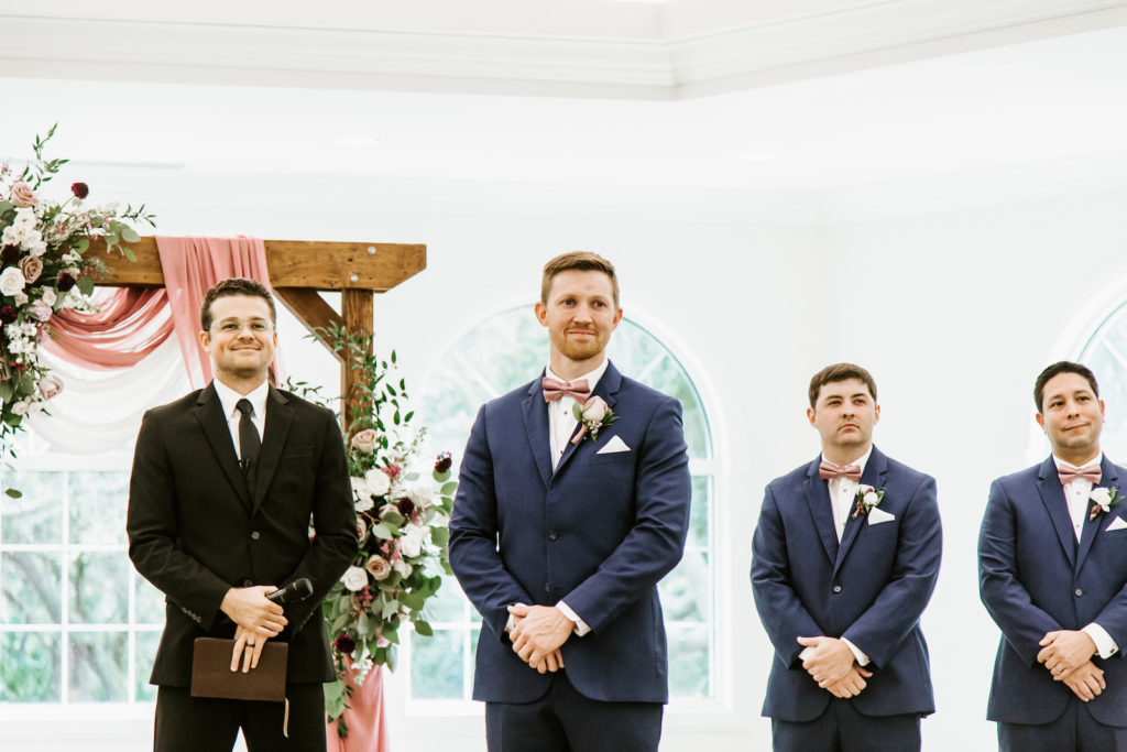 Groom Seeing His Bride for the First Time | St. Pete Wedding Venue Harborside Chapel | Groom and Groomsmen in Navy Blue Suits with Blush Pink Dusty Rose Mauve Bow Ties