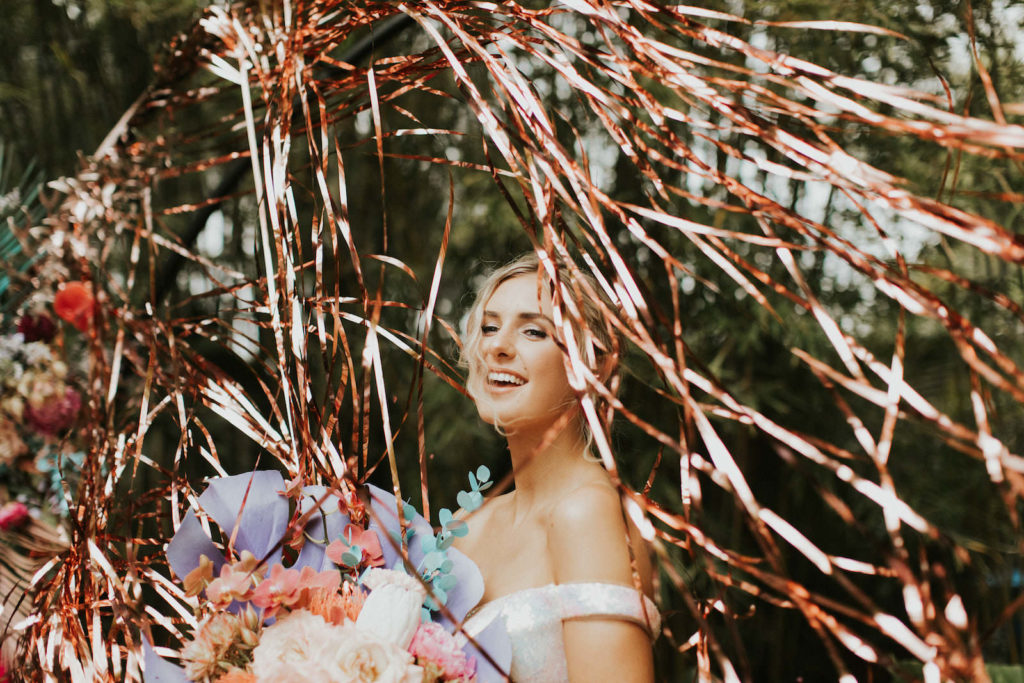 Iridescent Pastel 90's Wedding Inspiration | Wedding Arch Backdrop with Rose Gold Tinsel Curtain and Pastel Bouquet with Painted Leaves | Bridal Portrait with Shimmer Silver Wedding Dress