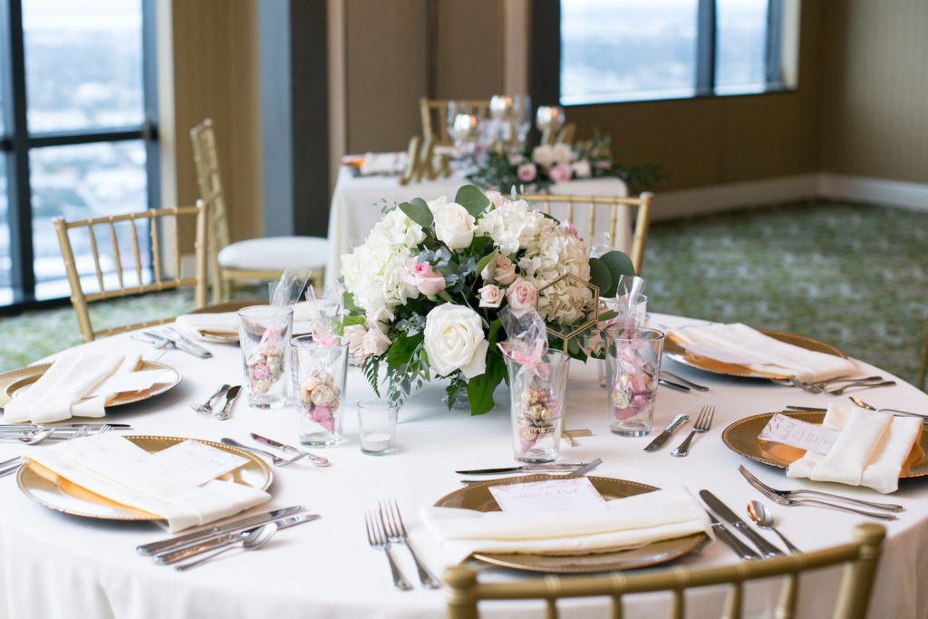 Indoor Wedding Reception at Downtown Tampa wedding Venue The Tampa Club | White Reception Table Linens with Gold Chiavari Chairs and Chargers and Centerpieces of White Hydrangea and White and Blush Pink Roses with Eucalyptus Greenery | Pint Glass Wedding Favors | Carrie Wildes Photography
