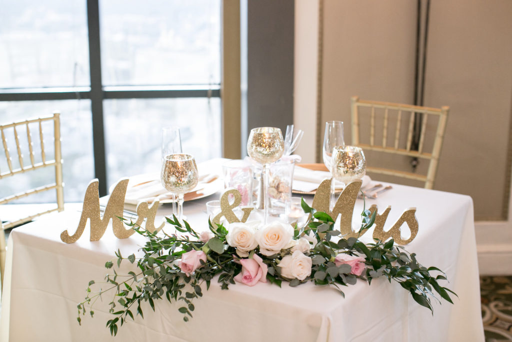 Wedding Sweetheart Table with White Linen and Gold Chiavari Chairs with White and Blush Pink Roses and Eucalyptus Greenery and Gold Mercury Glass Candles with Gold Glitter Mr and Mrs Tabletop Sign