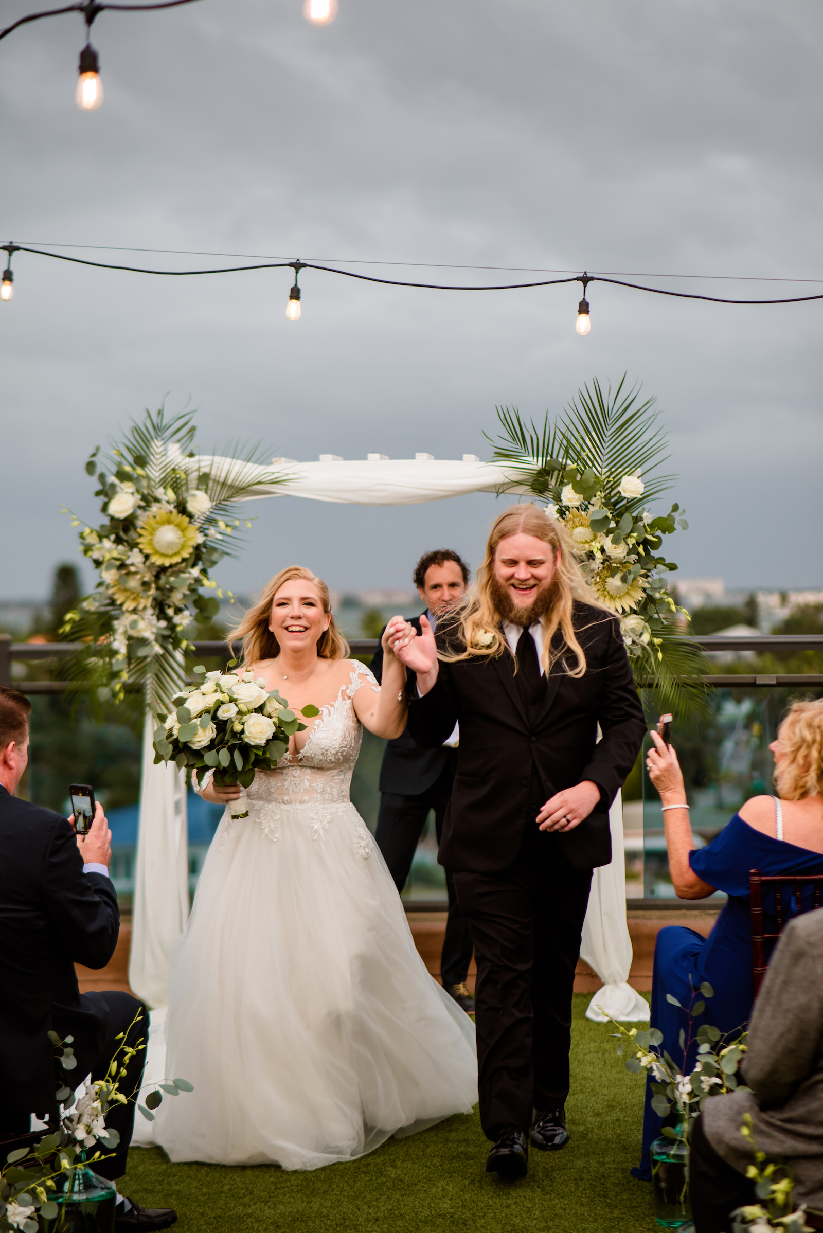 Florida Bride and Groom Wedding Ceremony Exit, Boho Neutral Tropical Wedding Ceremony Decor, Arch with Lush Floral Arrangements, Eucalyptus, King Proteas, White Florals and Palm Fronds | Tampa Bay Wedding Planner Perfecting the Plan | Wedding Florals Iza's Flowers