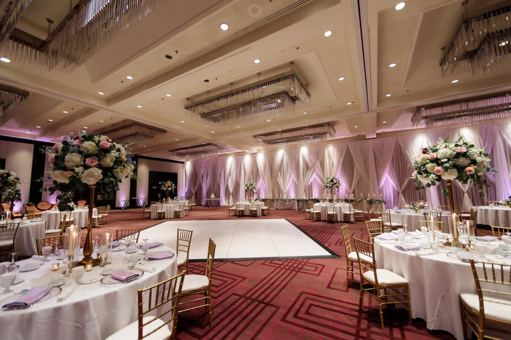 Tampa Hotel Wedding Reception at Hilton Downtown Tampa Ballroom | White Table Linens with Gold Chiavari Chairs and Tall Gold Centerpieces of White Hydrangea, Blush Pink and Deep Red Roses and Dusty Blue Eucalyptus Greenery | White Dance Floor and White Pipe and Drape Room Divider Wall with LED Uplighting | Monarch Events and Designs