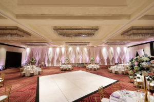 Tampa Hotel Wedding Reception at Hilton Downtown Tampa Ballroom | White Table Linens with Gold Chiavari Chairs and Tall Gold Centerpieces of White Hydrangea, Blush Pink and Deep Red Roses and Dusty Blue Eucalyptus Greenery by Tampa Wedding Florist Monarch Events and Design | White Dance Floor and White Pipe and Drape Room Divider Wall with LED Uplighting