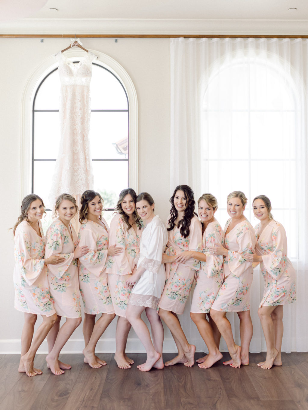 Tampa Bride and Bridesmaids in Blush Pink Floral Matching Robes, Lace and Illusion Wedding Dress Hanging in Window | Wedding Hair and Makeup Artist Femme Akoi