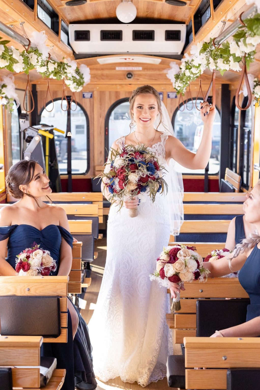 Bride and Bridesmaids on Way to Wedding on Jolley Trolley in White Lace Wedding Dress and Red, Navy, Natural Floral Bouquet