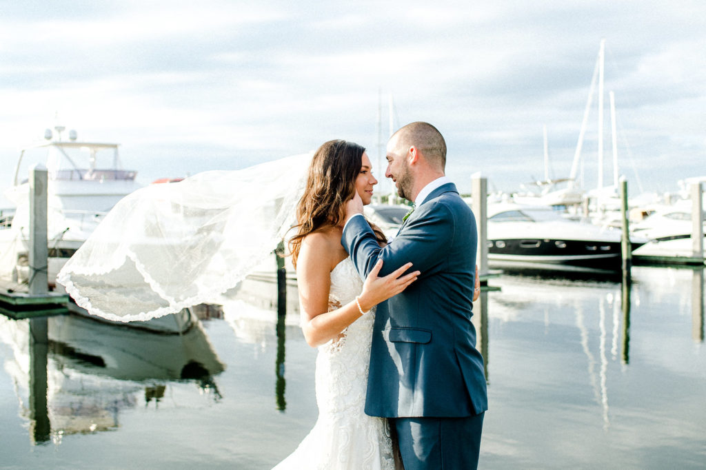 Bride and Groom Outdoor Portrait along Marina Dock at Tampa wedding venue Westshore Yacht Club | Lace Strapless Sweetheart Scalloped Edge Train Wedding Dress Bridal Gown with Elbow Length Lace Edge Veil | Groom Wearing Classic Navy Suit | Dewitt for Love Photography