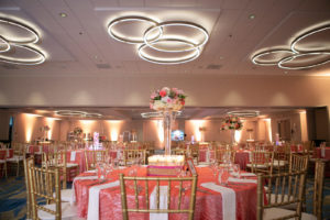 Tampa Clearwater Beach Indian Wedding at Hilton Clearwater Beach Wedding Venue | Ballroom Hotel Wedding Reception Tables with Gold Chiavari Chairs and Coral Pink Table Cloth Linens and White Napkins | Tall Floral Centerpieces with Pink Peach Coral Roses and White Hydrangea surrounded by Floating Candles | Hilton Clearwater Beach