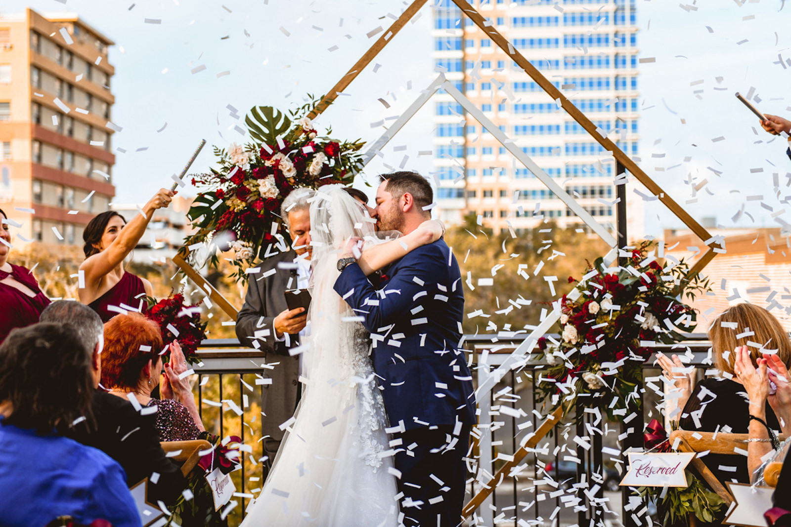 Bride and Groom Exchanging Firs Kiss as Bride and Groom During Rooftop Ceremony in Front of Geometric Sculpture Confetti Photo | Tampa Bay Wedding Planner Special Moments Event Planning | Downtown St. Pete Wedding Venue Red Mesa Events