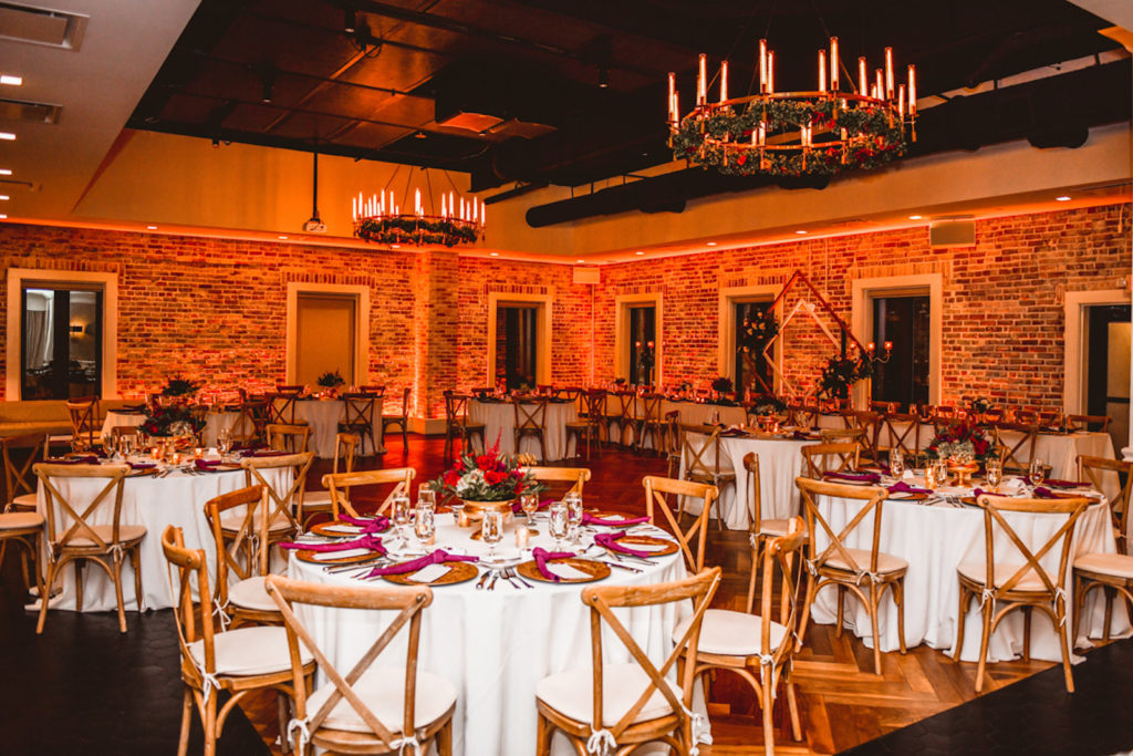 Botanical Inspired Wedding Reception Decor, Wooden Cross Back Chairs, Burgundy Red Linen Napkins, Gold Chargers, Low Floral Centerpieces, Gold Round Candle Chandeliers with Greenery and Red Roses Wreath | Tampa Bay Wedding Planner Special Moments Event Planning | Downtown St. Pete Wedding Venue Red Mesa Events