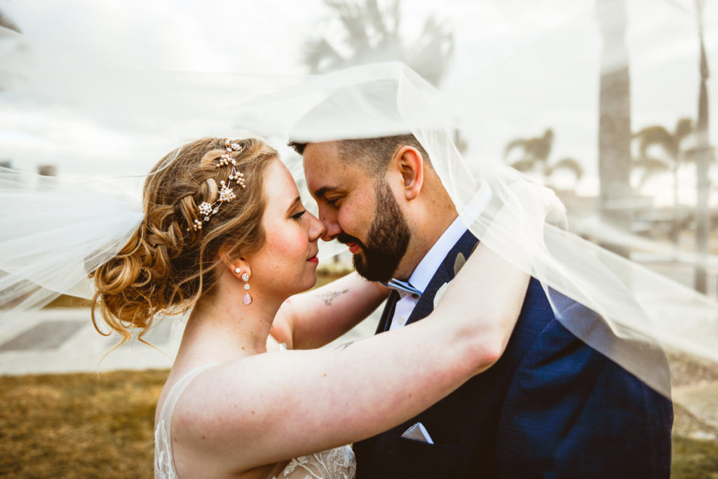 Boho Florida Bride with Braided Updo and Flowers Intimate Photo with Groom Under Veil | Tampa Bay Wedding Hair and Makeup Femme Akoi