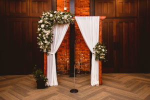 Industrial Wedding Reception Decor, Wooden Arch with White Linen Draping, Lush Greenery, Eucalyptus, Ivory Roses Floral Arrangement | Tampa Wedding Venue Armature Works