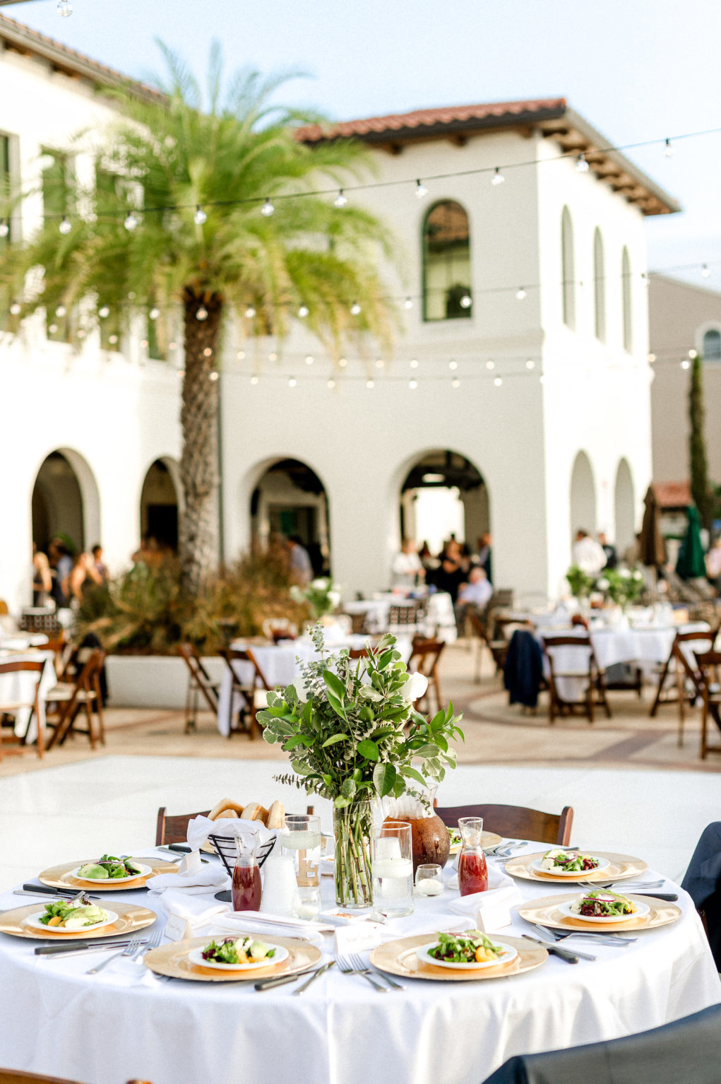 Outdoor wedding Reception at Tampa wedding Venue Westshore Yacht Club | Round tables with white linens and mahogany wood folding chairs with gold charger plates and greenery centerpieces