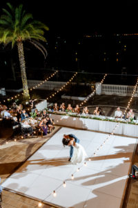 Bride and Groom First Dance on white Dance Floor under Canopy String Lights | Outdoor wedding Reception at Tampa wedding Venue Westshore Yacht Club | Long head table with greenery garland centerpieces