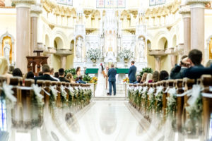 Bride and Groom Exchanging Vows during Downtown Tampa Wedding Ceremony at Sacred Heart Catholic Church | Church Ceremony Aisle with Greenery | Groom Wearing Classic Navy Suit | Dewitt for Love Photography