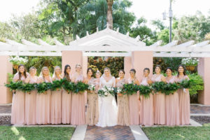 Tampa Bride Wearing Lace and Illusion Long Sleeve Wedding Dress with Bridesmaids in Blush Pink Dresses Holding Greenery Bouquets in Courtyard St. Pete Wedding Venue The Vinoy | Wedding Planner Parties A'la Carte | Wedding Florist Bruce Wayne Florals