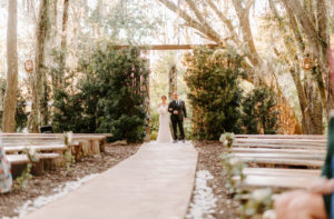 Bride Walking Down Aisle with Father during Outdoor Wedding Ceremony with Wood Benches at Plant City Wedding Venue Florida Rustic Barn Weddings