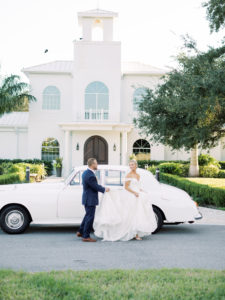 Timeless Florida Groom Holding Train of Bride's Dress in Front of White Vintage Car | Safety Harbor Traditional Wedding Ceremony Venue Harborside Chapel
