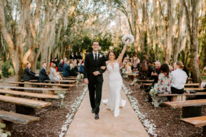 Bride and Groom Exit during Outdoor Wedding Ceremony at Plant City Wedding Venue Florida Rustic Barn Weddings | Groom Wearing Classic Black Suit Tux | White Peony Bridal Bouquet | Sheath Illusion Lace Bridal Gown wedding Dress