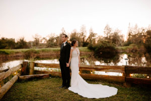 Outdoor Bride and Groom Sunset Portrait at Florida Lake | Groom Wearing Classic Black Suit Tux | White Peony Bridal Bouquet | Sheath Illusion Lace Bridal Gown wedding Dress