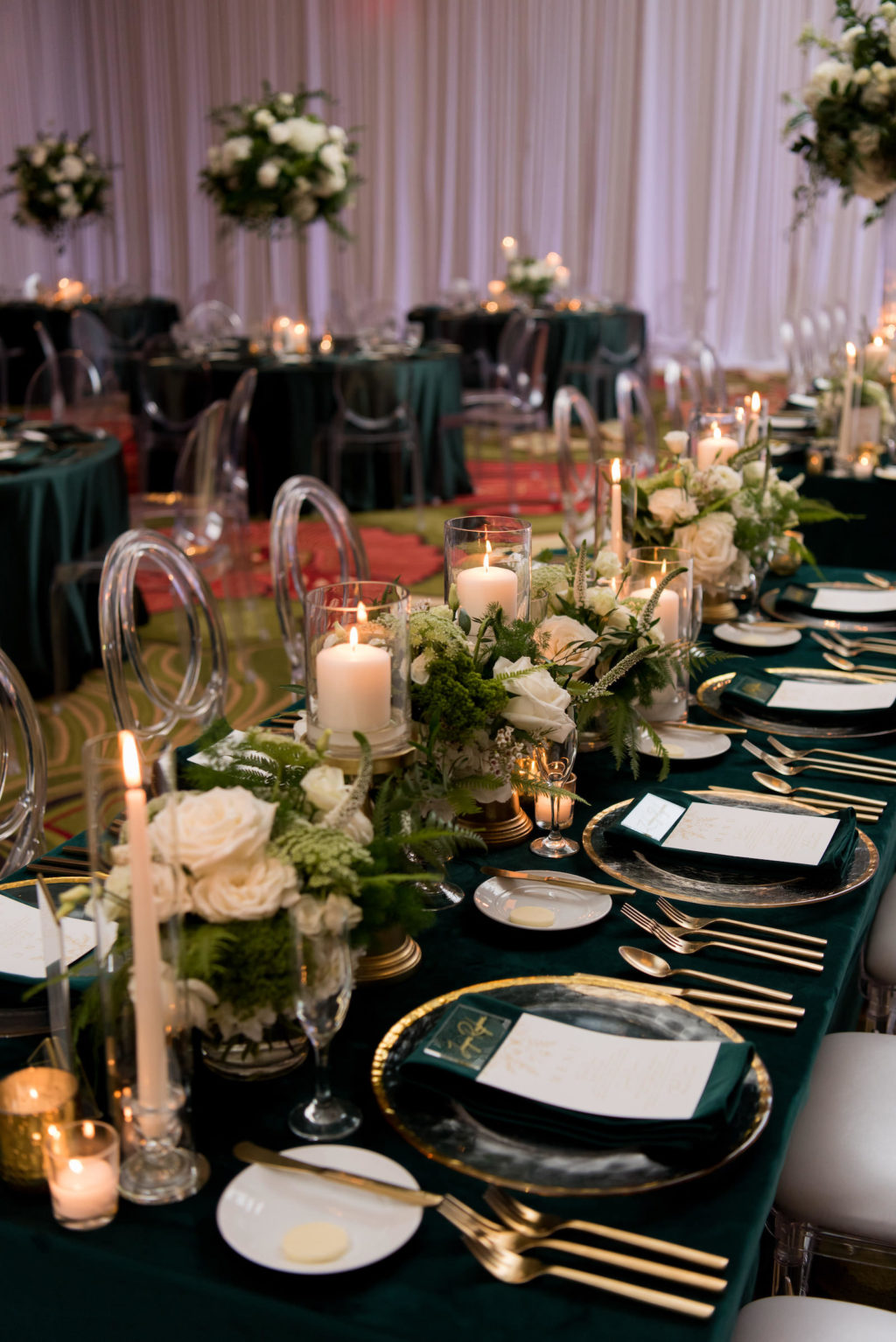 Elegant Wedding Reception Decor, Long Feasting Table with Emerald Green Linens, Gold Rimmed Chargers and Flatware Candles, Low White Roses and Greenery Floral Arrangements, Acrylic Chiavari Chairs | Tampa Bay Wedding Planner Parties A'la Carte | Wedding Chairs, Chargers, Chairs and Flatware Rentals A Chair Affair | Wedding Florist Bruce Wayne Florals
