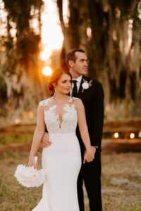 Outdoor Bride and Groom Sunset Portrait | Groom Wearing Classic Black Suit Tux | White Peony Bridal Bouquet | Sheath Illusion Lace Bridal Gown wedding Dress