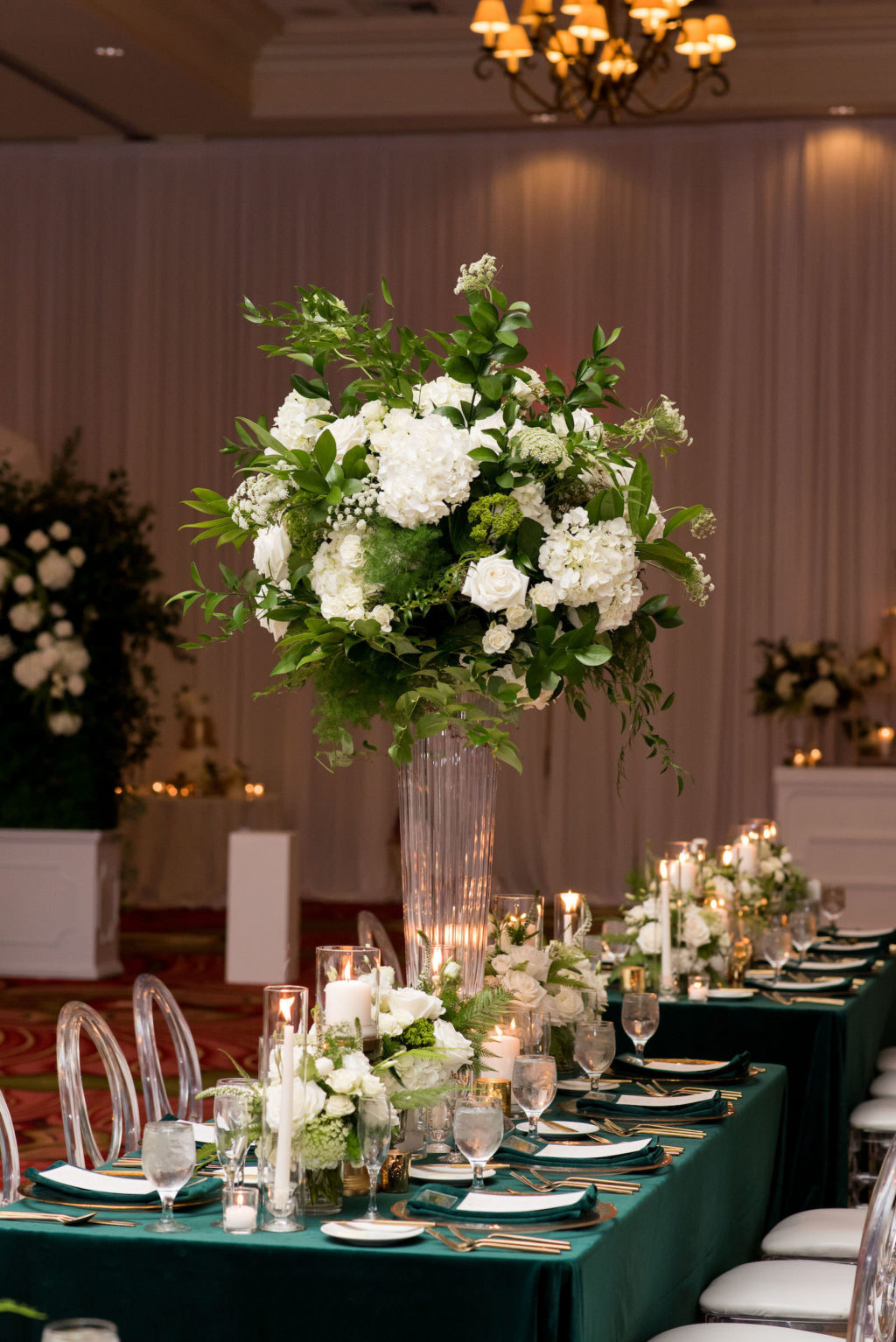 Elegant Wedding Reception Decor, Long Feasting Table with Emerald Green Linens, Gold Rimmed Chargers and Flatware Candles, Tall White Roses and Greenery Floral Arrangements, Acrylic Chiavari Chairs | Tampa Bay Wedding Planner Parties A'la Carte | Wedding Chairs, Chargers, Chairs and Flatware Rentals A Chair Affair | Wedding Florist Bruce Wayne Florals