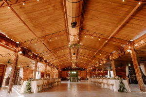 Wood Barn Reception at Plant City Wedding Venue Florida Rustic Barn Weddings | Long Feasting Tables with White Linens and Eucalyptus Greenery Garland Centerpieces and Wood Cross Back Chairs under a Canopy of String Lights
