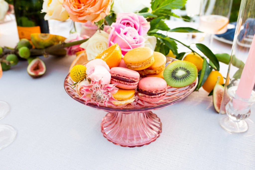 Citrus Inspired Florida Wedding Reception Decor Details, Pink Glass Cake Stand with Bright Macaroon Cookies mixed with Fresh Organic Fruit, Kiwi, Oranges, Pomegranates, Kumquats, With Pink, White and Orange Roses