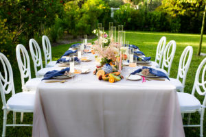 Tampa Bay Garden Inspired Intimate Wedding Ceremony at Sarasota Garden Club, Florida Micro Wedding Style Shoot with Silver Linens, White Circle Back Chairs, Citrus Orange and Peach Florals, Pops of Dark Blue Blue, Gold Flatware, Light Pink Florals in Outdoor Venue