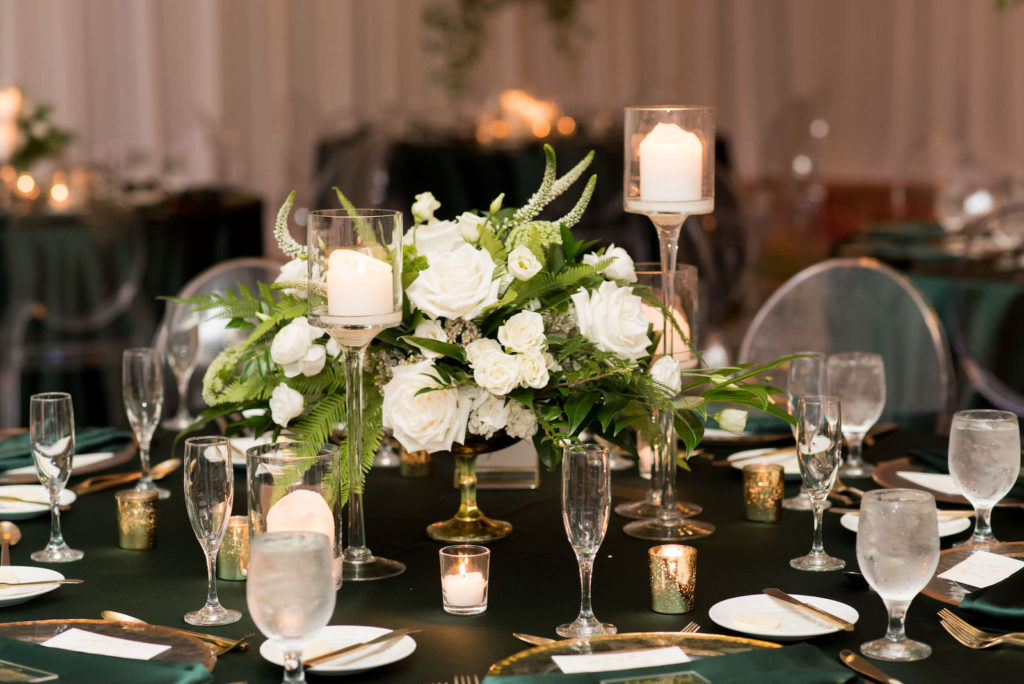 Elegant Wedding Reception Decor, Table with Emerald Green Linens, Gold Rimmed Chargers and Flatware Candles, Low White Roses and Greenery Floral Arrangements, Acrylic Chiavari Chairs | Tampa Bay Wedding Planner Parties A'la Carte | Wedding Chairs, Chargers, Chairs and Flatware Rentals A Chair Affair | Wedding Florist Bruce Wayne Florals