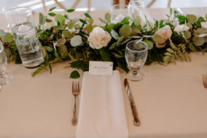 Long Feasting Tables with White Linens and Rose and Eucalyptus Greenery Garland Centerpieces with Floating Candles and White Napkins
