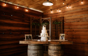 Rustic Plant City Wedding Wood Barrel Cake Table with Framed Engagement Photos | Three Tier Buttercream Wedding Cake with Fresh Flowers and Gold Calligraphy Cake Topper