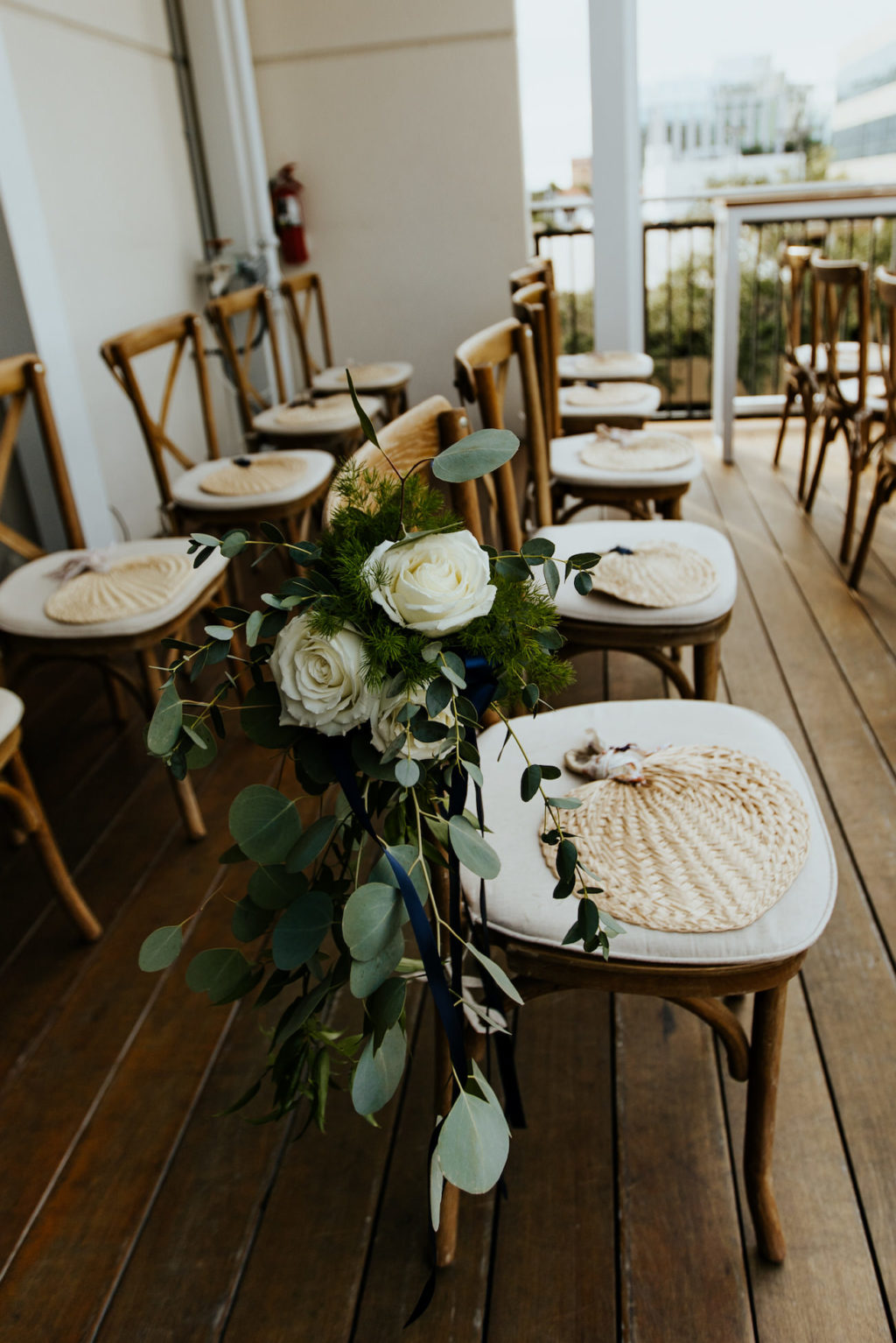 Rooftop Wedding Ceremony with Wood Cross Back Chairs and Rattan Straw Woven Hand Fans | Ceremony Aisle Floral Marker Arrangements with White Roses and Eucalyptus Greenery