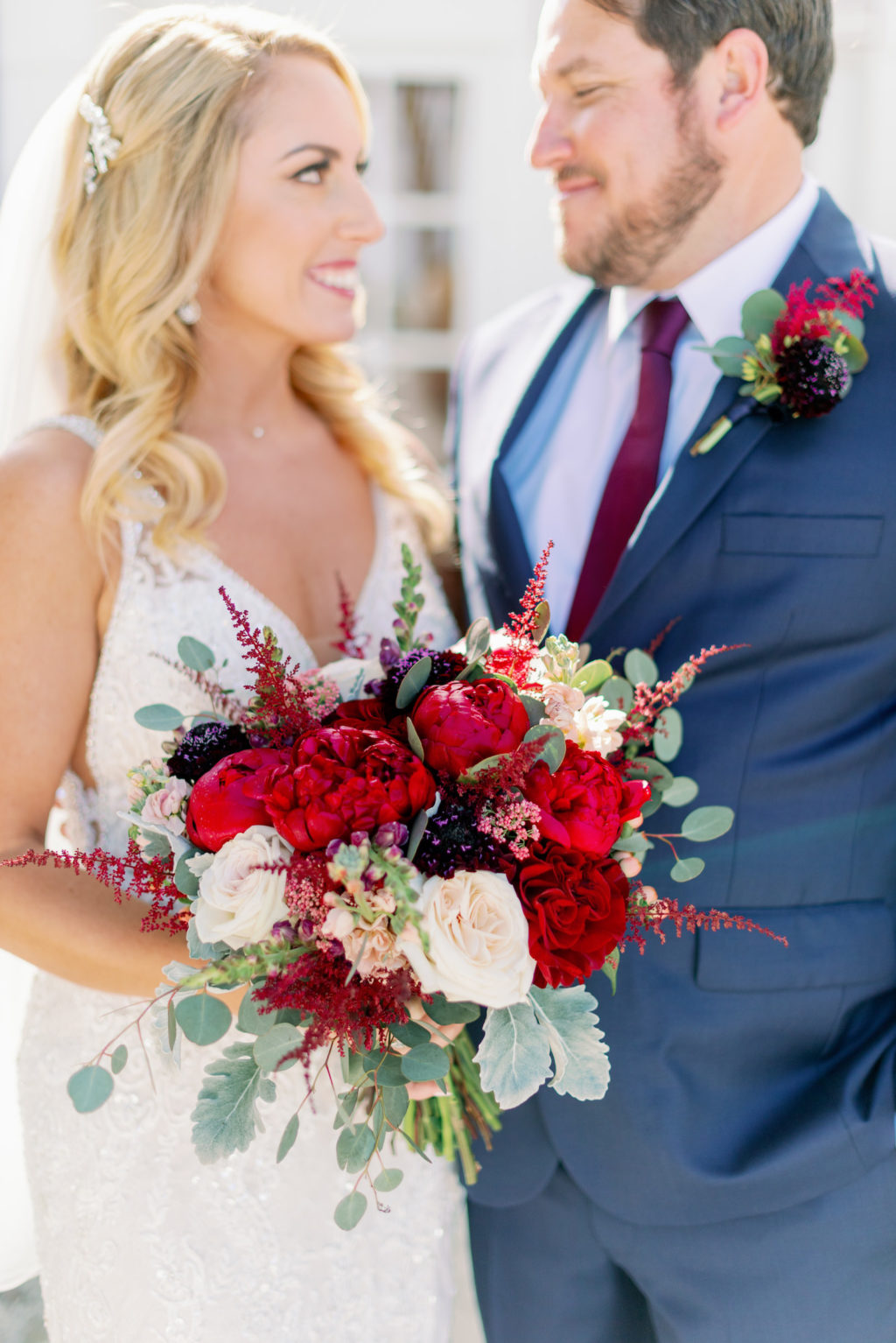 Romantic Rustic Glam Bride in Lace Wedding Dress Holding Red, Ivory and Greenery Floral Bouquet and Groom in Blue Suit | Tampa Bay Wedding Hair and Makeup Michele Renee the Studio