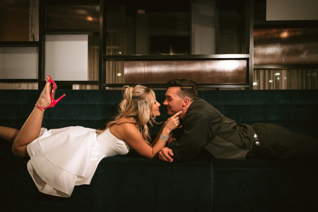 Urban and Edgy Bride in Short Wedding Dress and Red Wedding Shoes, Groom in Black Dress Pants and Shirt with Gray Vest Laying on Couch | Tampa Bay Wedding Photographer Bonnie Newman Creative | Wedding Venue Aloft/ Element Midtown Tampa | Wedding Designer and Planner UNIQUE Weddings + Events | Wedding Dress Truly Forever Bridal | Wedding Hair and Makeup Adore Bridal Services | Wedding Jewelry Accessories International Diamond Center | Wedding Furniture Rental A Chair Affair