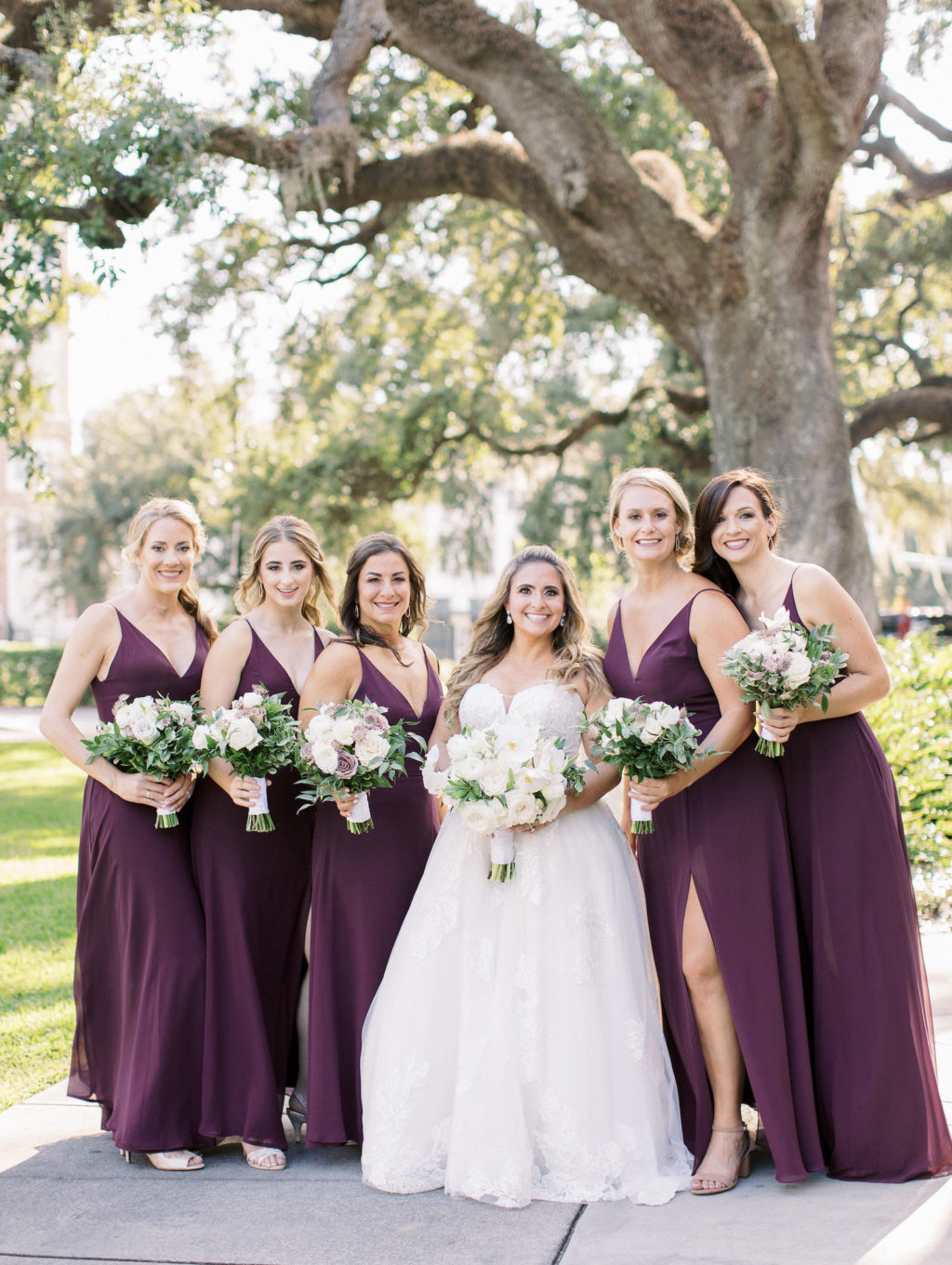 Tampa Bay Traditional Bride Wearing Ballgown Wedding Dress and Bridesmaids in Matching Plum Purple Dresses Holding White Floral Bouquets