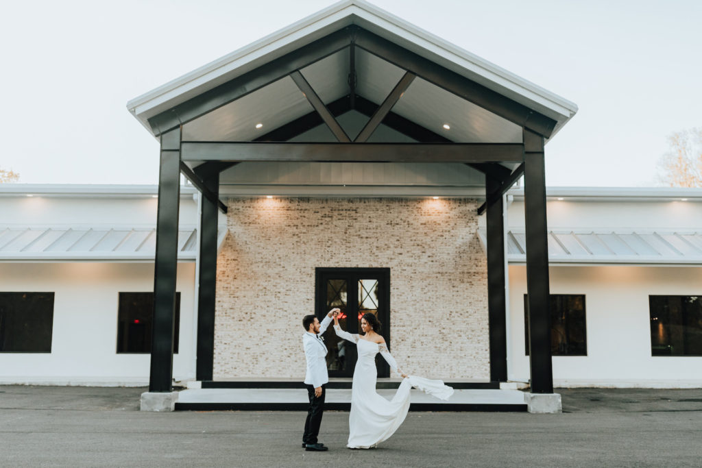 Outdoor Bride and Groom Portrait in front of Modern Industrial Farm House White Rock Canyon | Groom Wearing Classic Formal White Jacket with Black Lapel and Bow Tie | Off the Shoulder Lace Sleeve Sheath Wedding Gown Bridal Dress | Amber McWhorter Photography