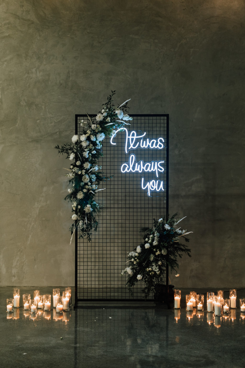 Black Modern Industrial Metal Screen Wedding Ceremony Backdrop Panel with Neon Sign, Candles, and Asymmetrical Floral Arrangements of White Roses and Winter Pine Greenery
