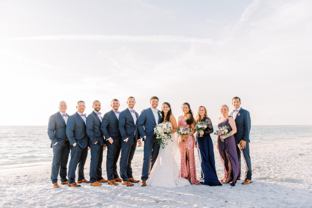 Sarasota Elegant Bride Holding Lush White Floral Bouquet, Bridesmaids in Mix and Match Purple Dresses, Groom and Groomsmen in Blue Suits Beach Sunset Photo | Tampa Bay Wedding Photographer Kera Photography