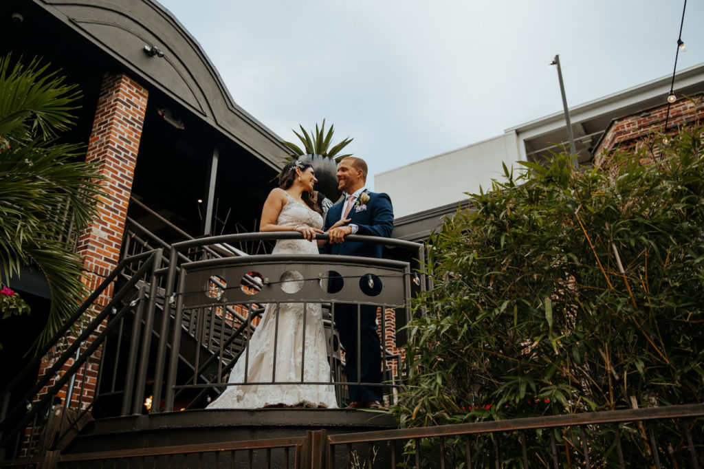 Bride and Groom Outdoor Staircase Portrait at Downtown St. Pete Florida Wedding at Red Mesa Events Rooftop | Bride Wearing Illusion Lace V Neck Sheath Wedding Dress Bridal Gown | Groom Wearing Classic Navy Blue Suit Tux