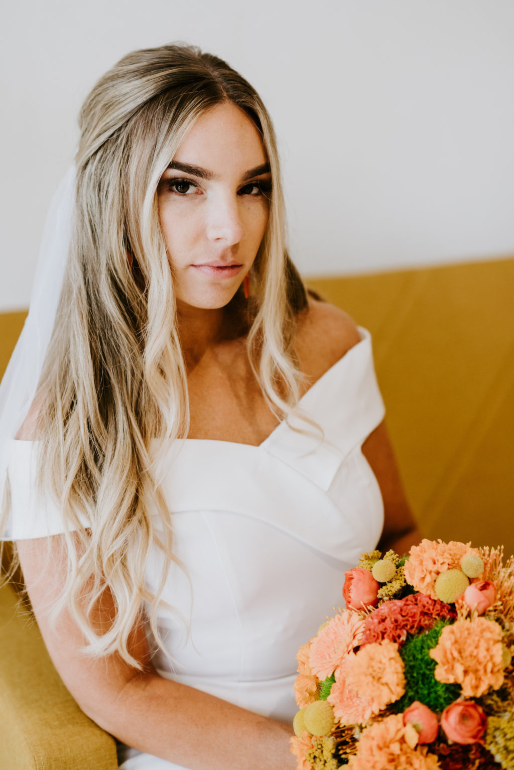Mid Century Modern Bride with Hair Half Up Wearing Off the Shoulder Wedding Dress Holding Retro Orange and Yellow Floral Bouquet