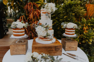 Natural Wedding Cake Display with Naked Cakes with White Roses and Greenery Decor on Stained Wooden Cake Stands