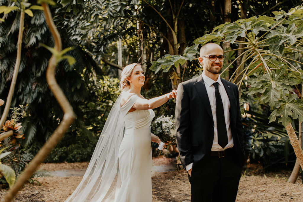 Classic Florida Bride and Groom First Look at Sunken Gardens in Downtown St. Petersburg, Bride Wearing White Fitted Off The Shoulder BHLDN Wedding Dress, Groom in Classic Black Suit and Tie | Tampa Bay Hair and Makeup Artist Femme Akoi Beauty Studios